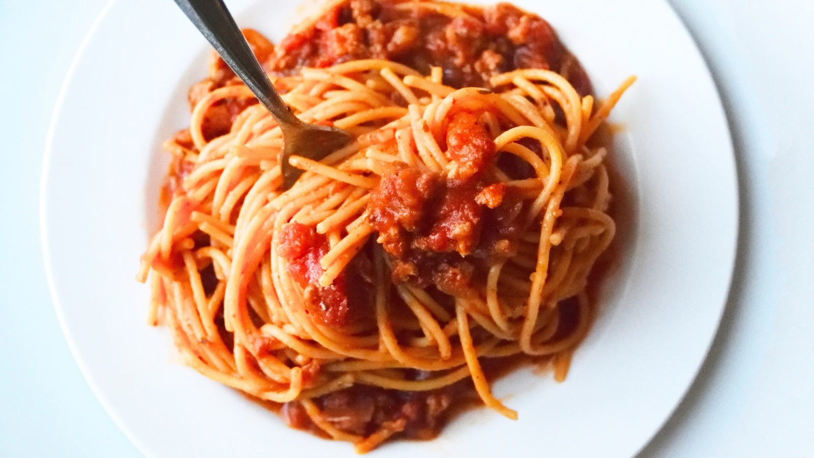 An overhead view of a white plate filled with a nest of spaghetti.