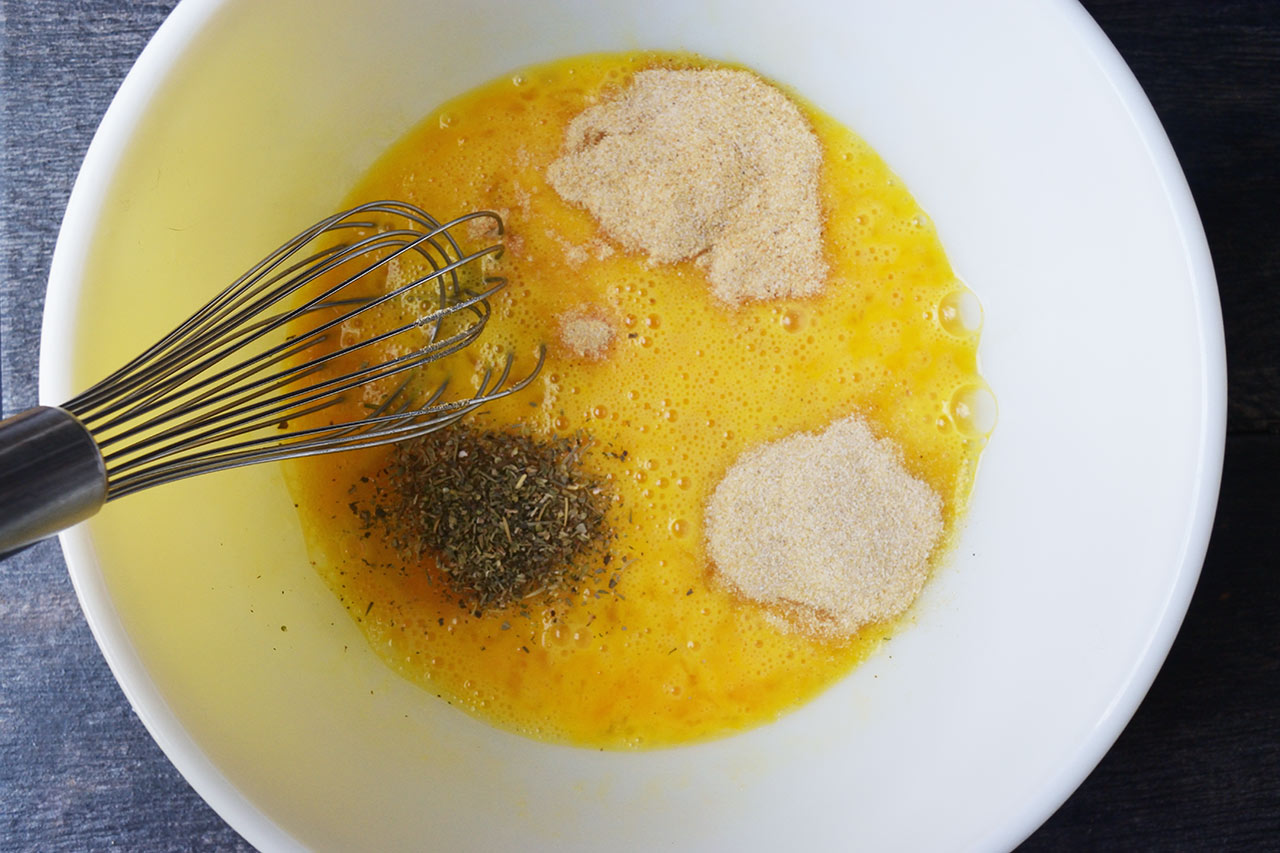 Spices added to whisked eggs in a mixing bowl.