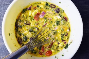 All the spinach quiche ingredients whisked together in a mixing bowl with a whisk.