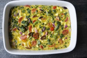 Raw quiche ingredients poured into an oiled casserole dish for baking.