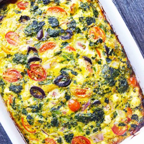 An overhead view of a white casserole dish filled with spinach quiche.