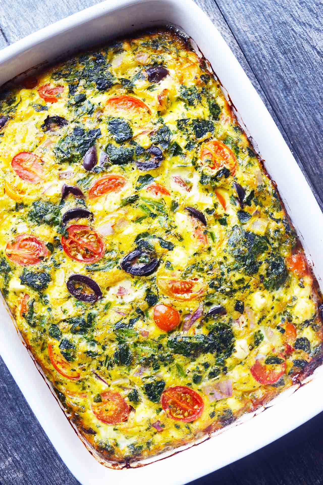 An overhead view of a white casserole dish filled with spinach quiche.