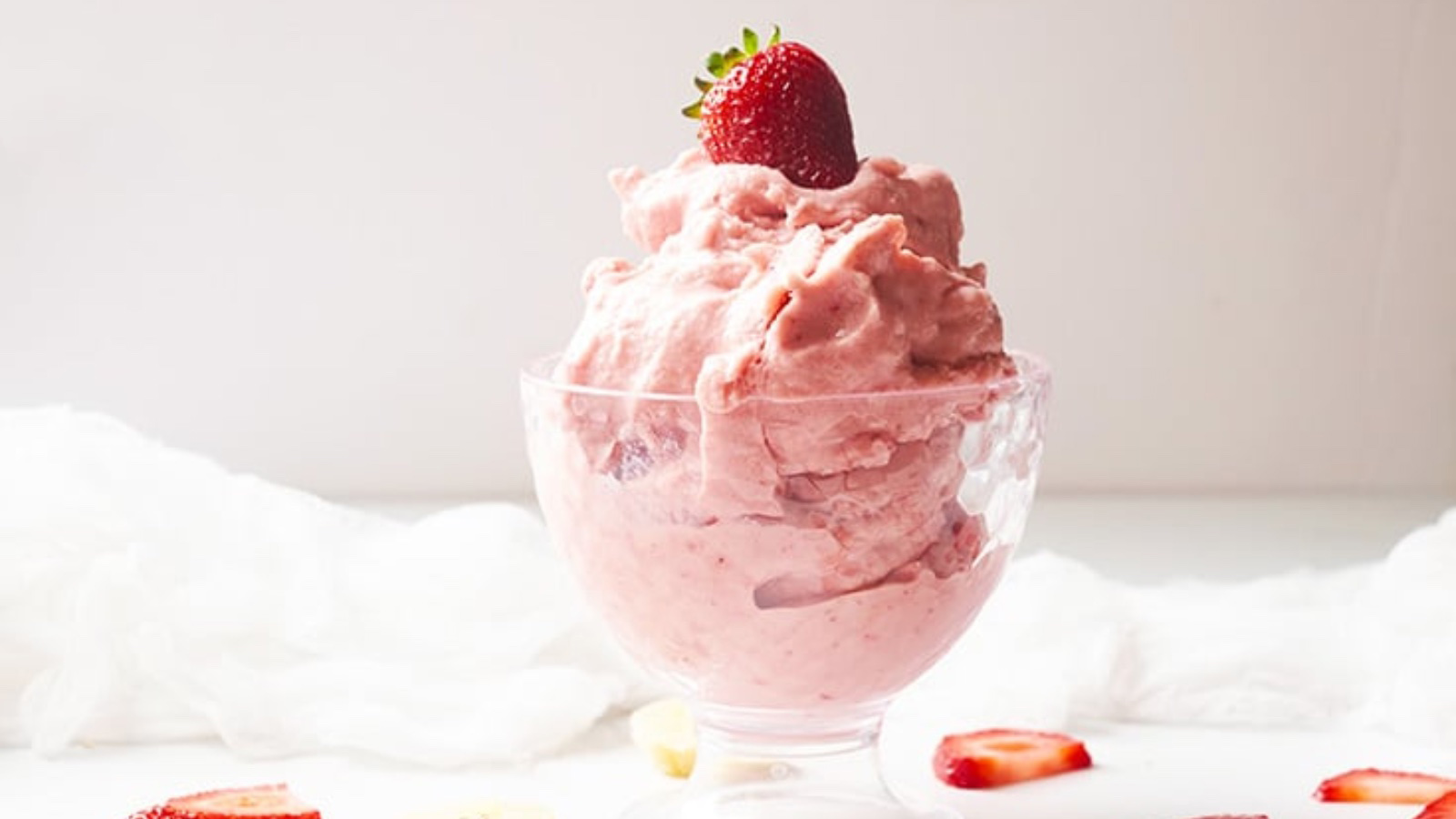 Strawberry ice cream piled high in a glass ice cream bowl and topped with a fresh strawberry.