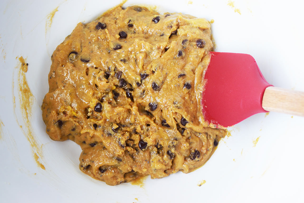 Mixed cookie batter sitting in a white mixing bowl with a red spatula.