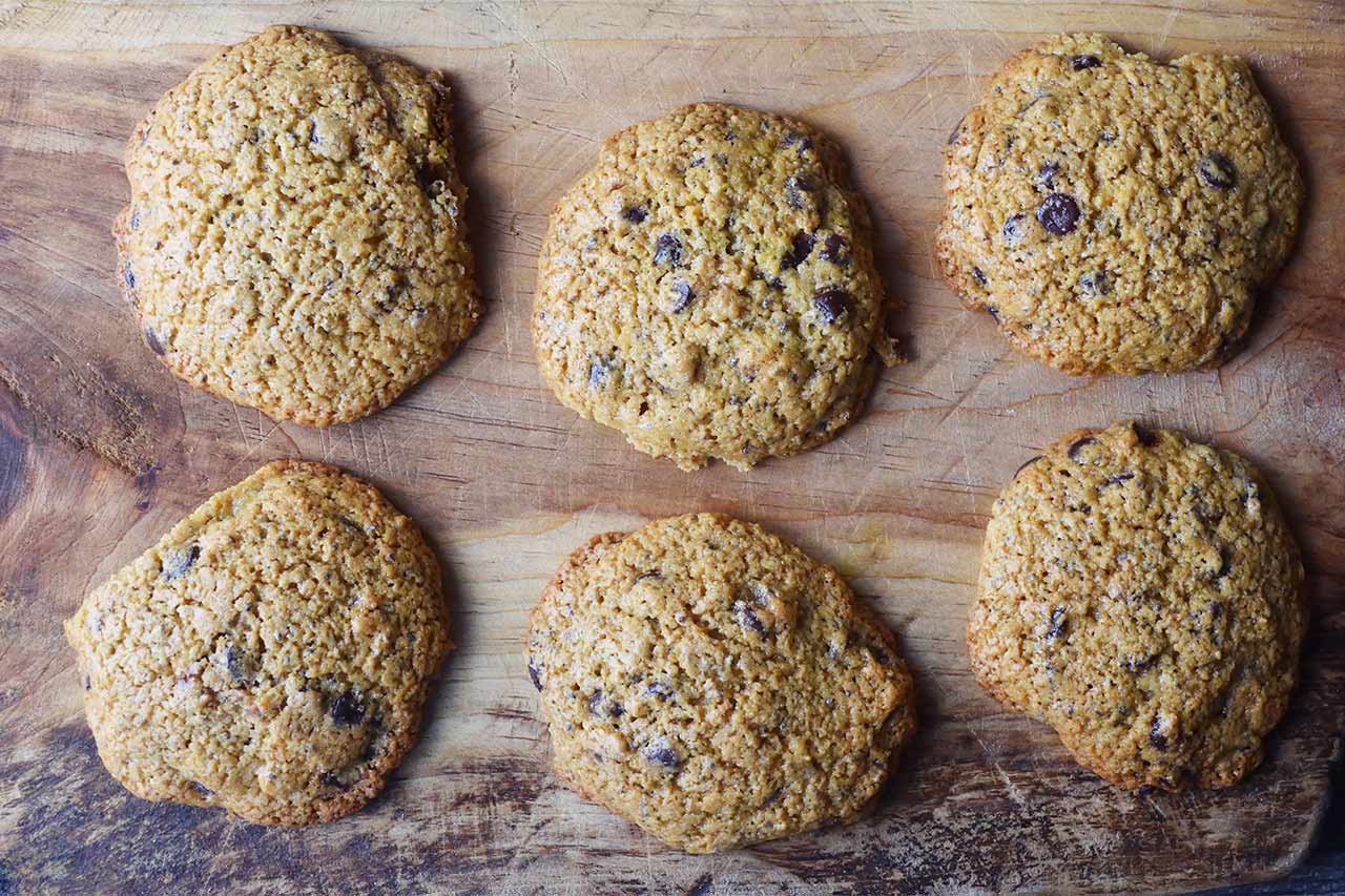 A closeup of six Superfood Chocolate Chip Cookies cooling on a wood cutting board.