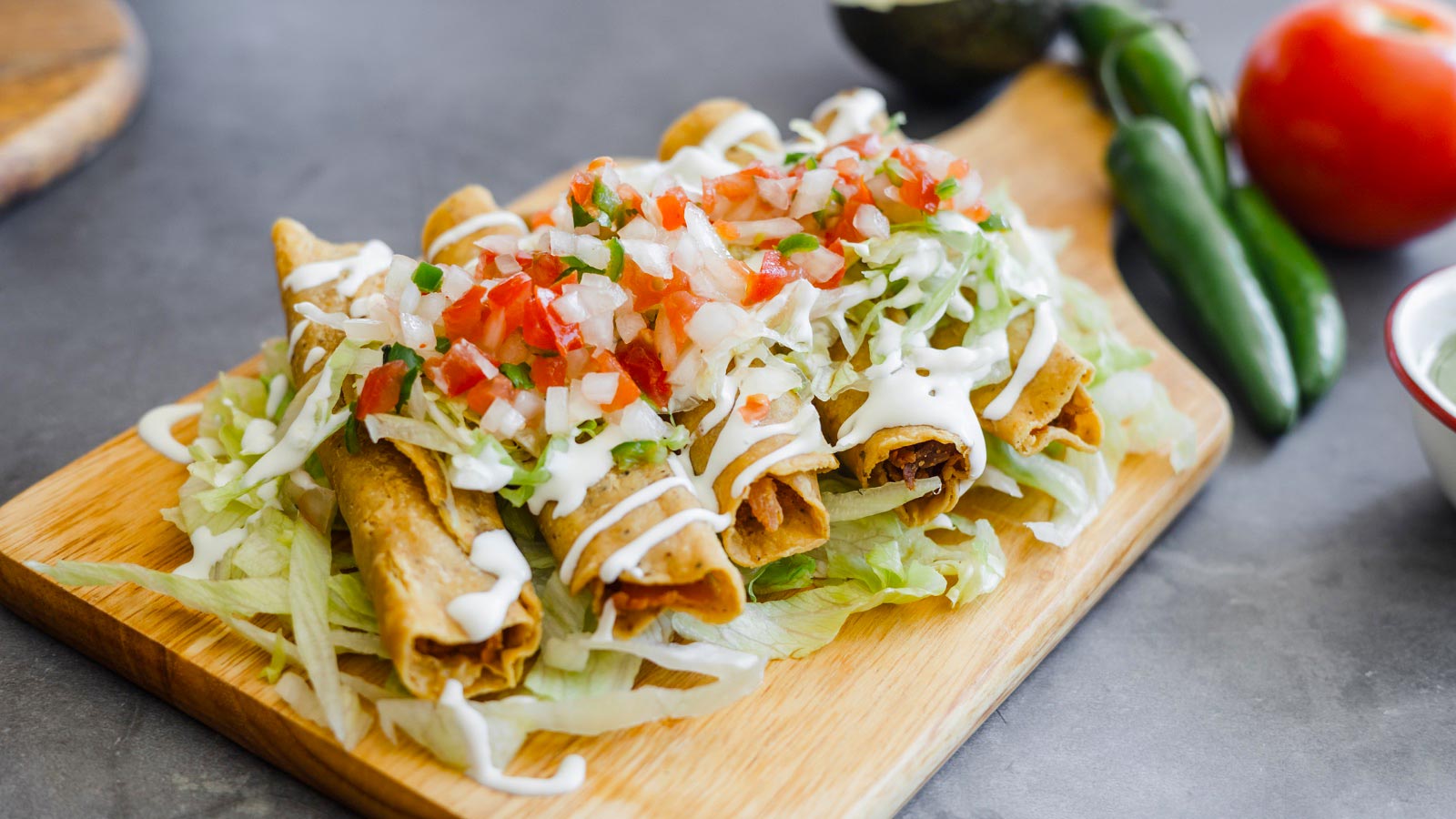 Mexican taquitos with chicken on a cutting board with toppings.