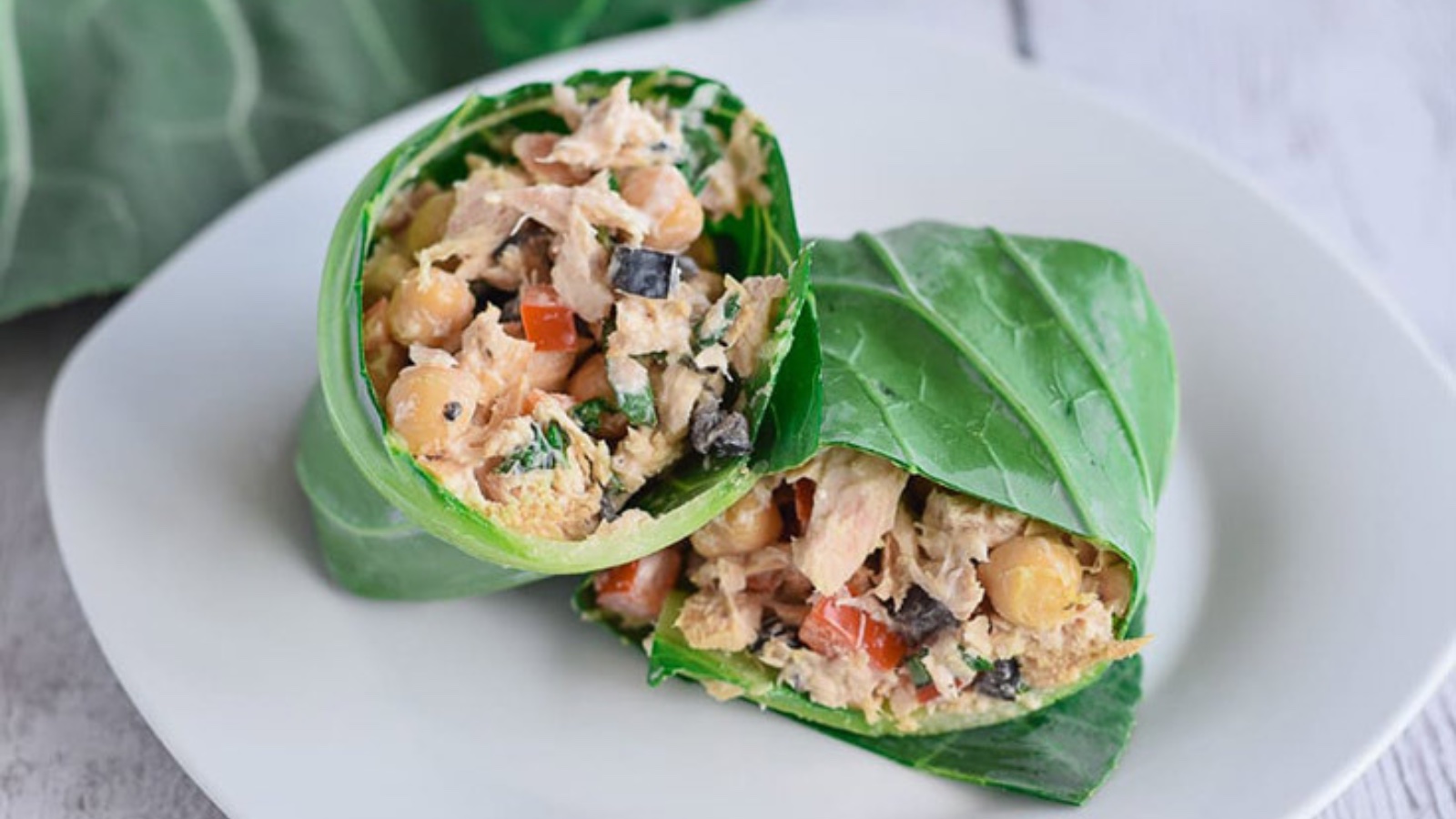 A tuna salad collard wrap cut in half and sitting on a white plate.