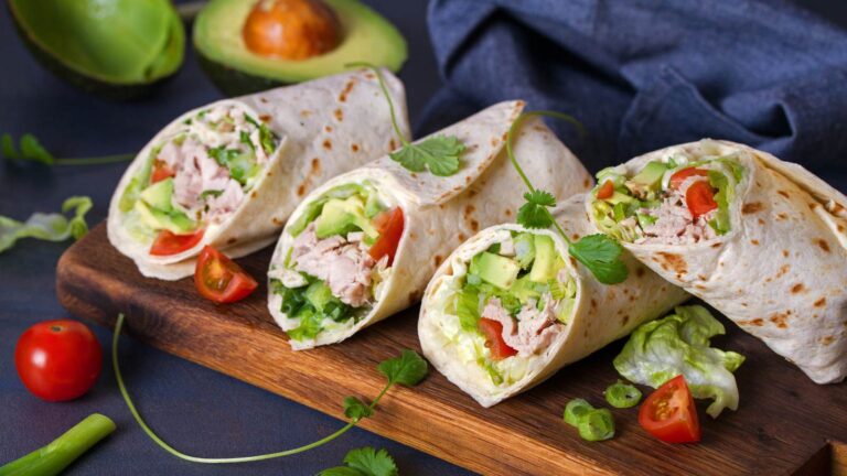 Turkey wraps with avocado, tomatoes and iceberg lettuce on chopping board.