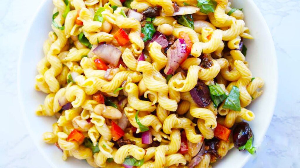 An overhead view of a white bowl filled with Tuscan pasta salad.