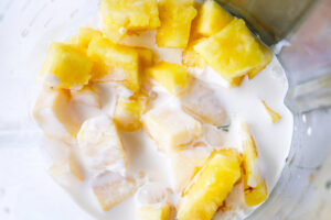 A blender tumbler with coconut milk added to fresh pineapple chunks in it.