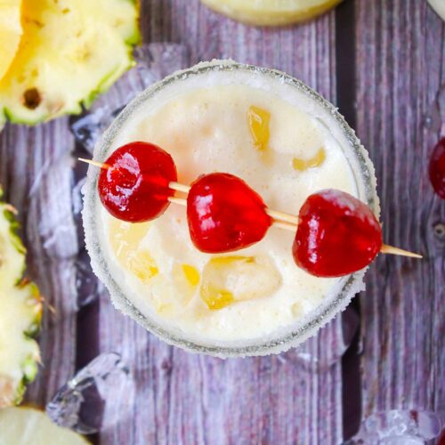 A directly overhead view of a glass full of Virgin Pina Colada with three cherries across the top on toothpicks.