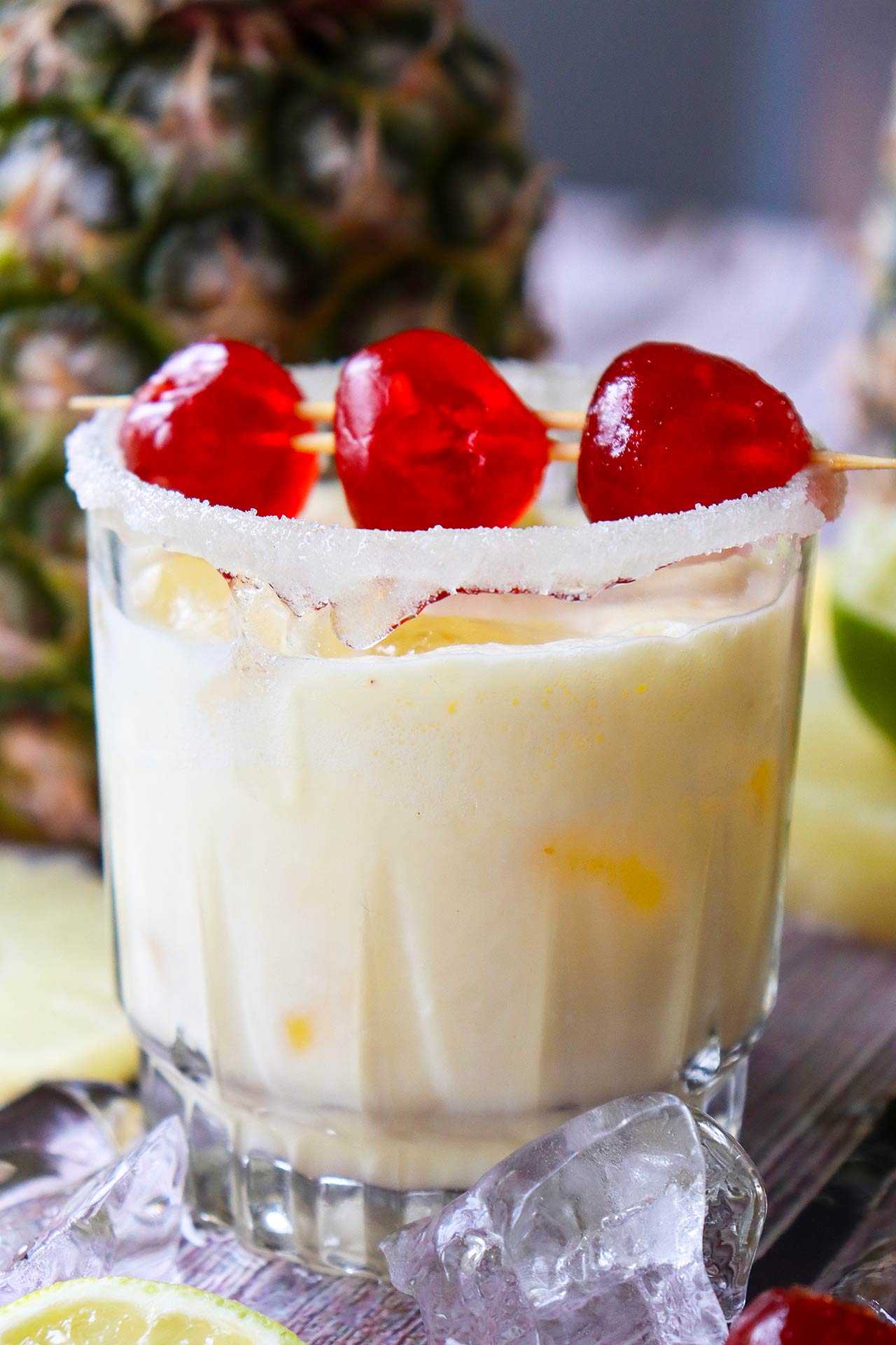 A Virgin Pina Colada in a glass with three cherries on a toothpick laid across the top of the glass.