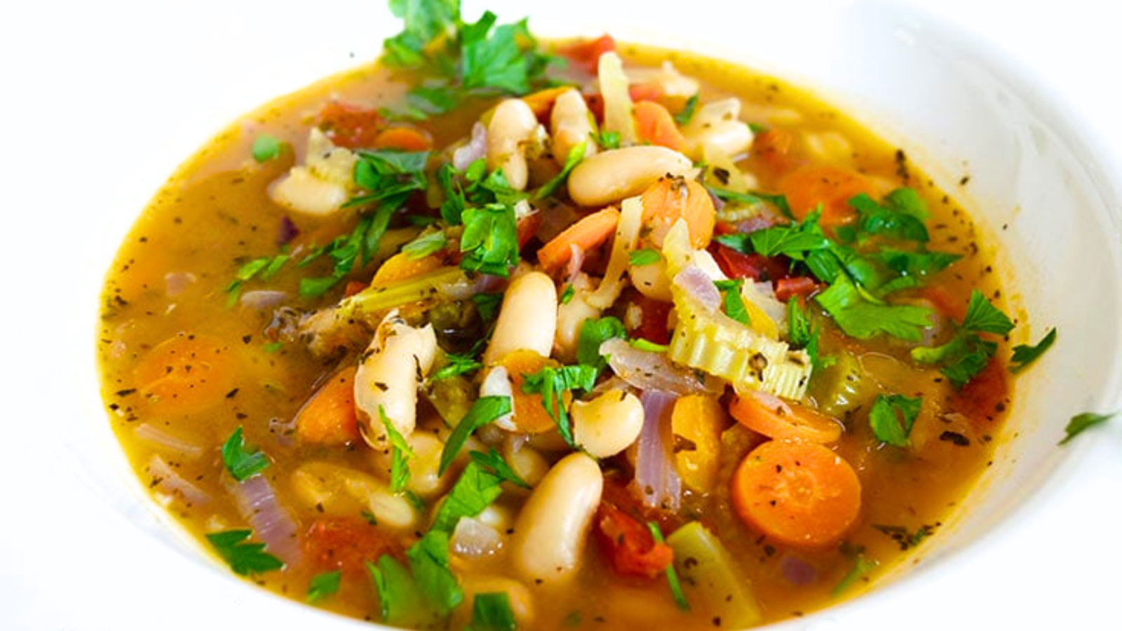 A white bowl hold a serving of white bean soup and is garnished with fresh parsley.