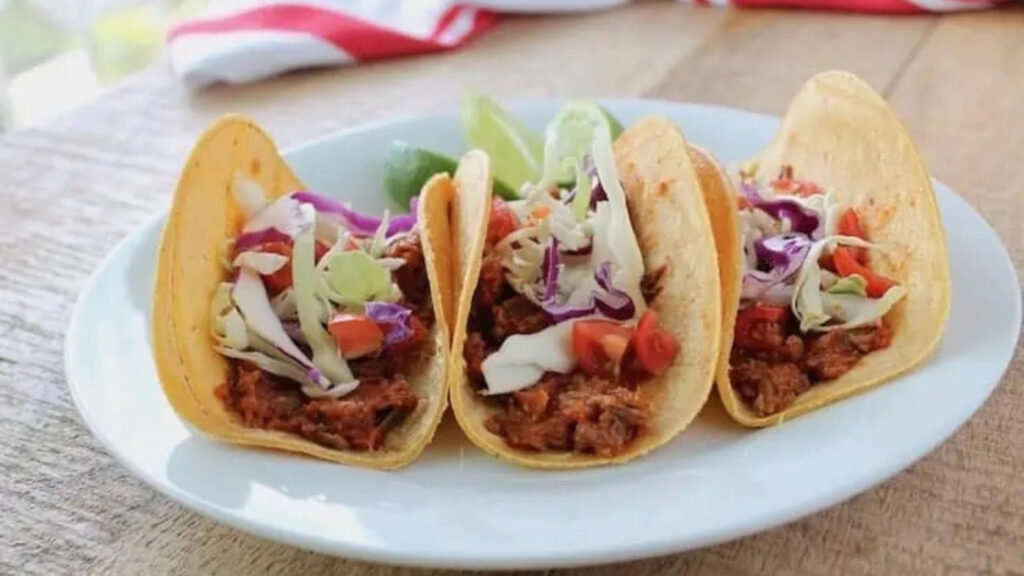Three tacos lined up on a white plate.