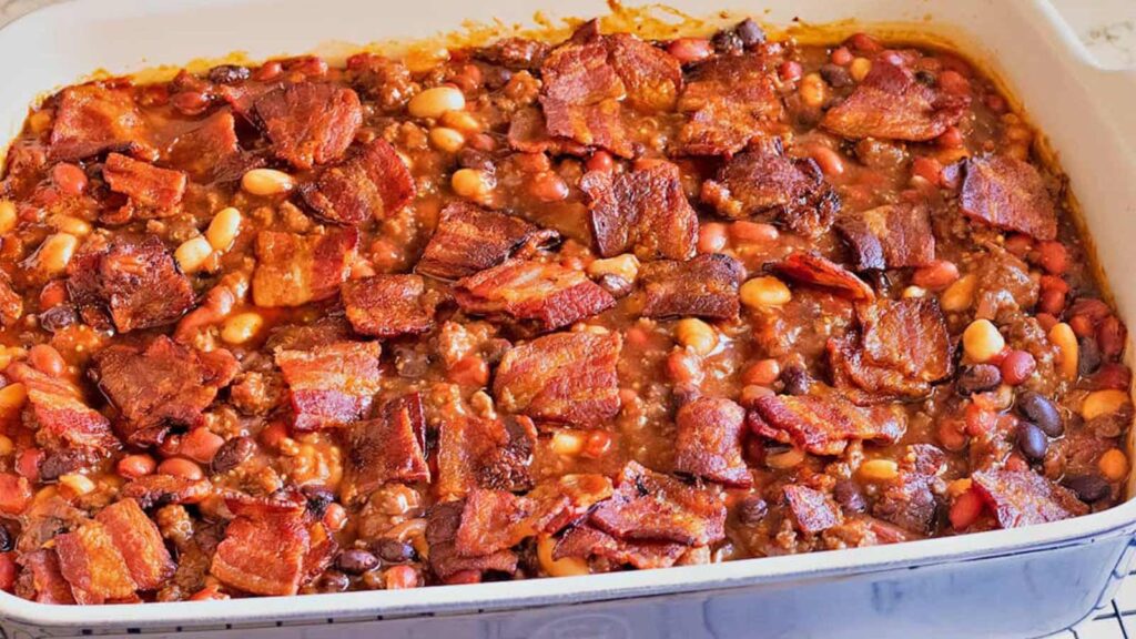 A white casserole dish filled with baked bean casserole topped with bacon pieces.