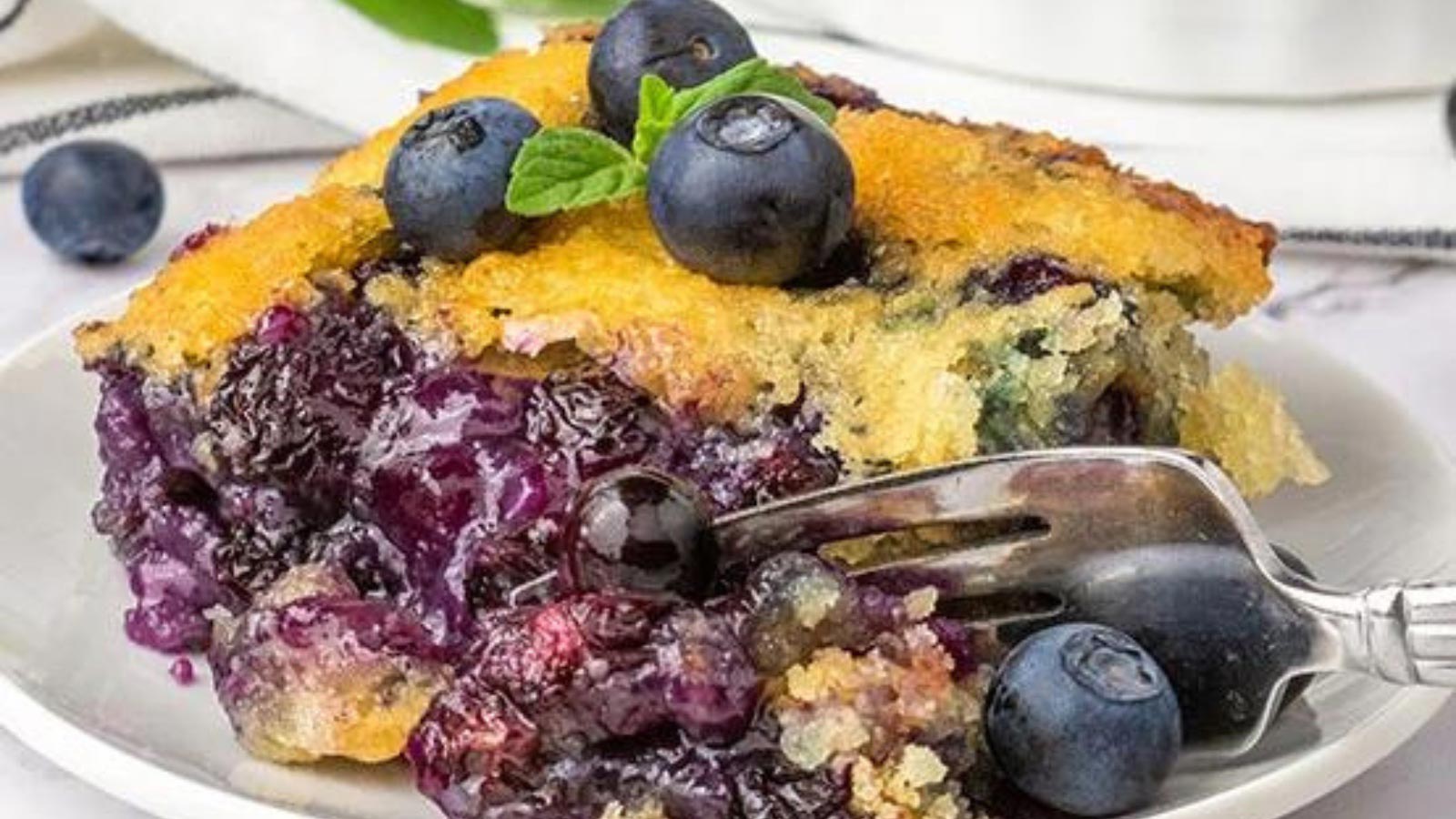 A closeup of a serving of blueberry cobbler on a white plate with a fork.