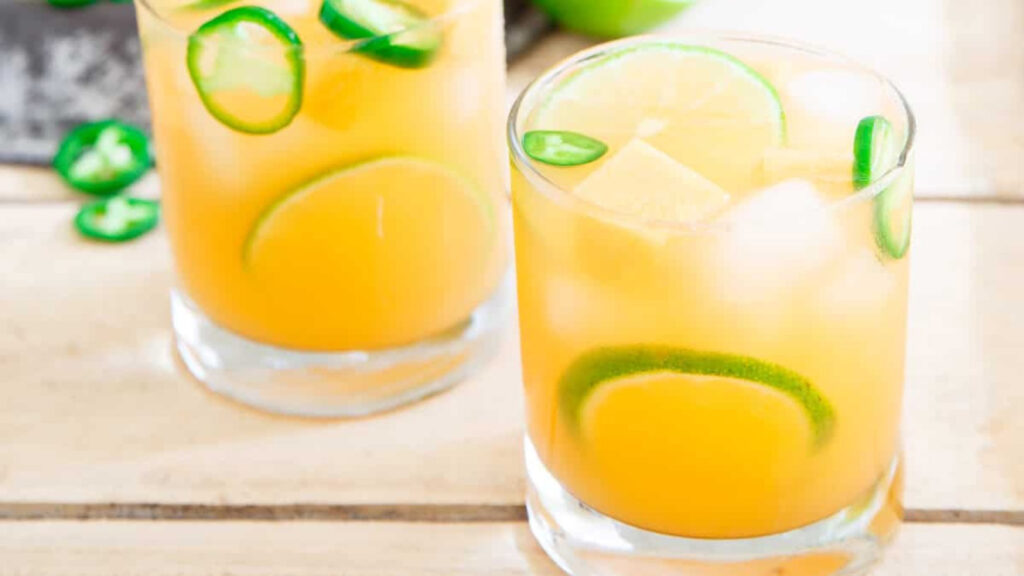 Two glasses of cantaloupe lime jalapeno agua fresca on a wood table.