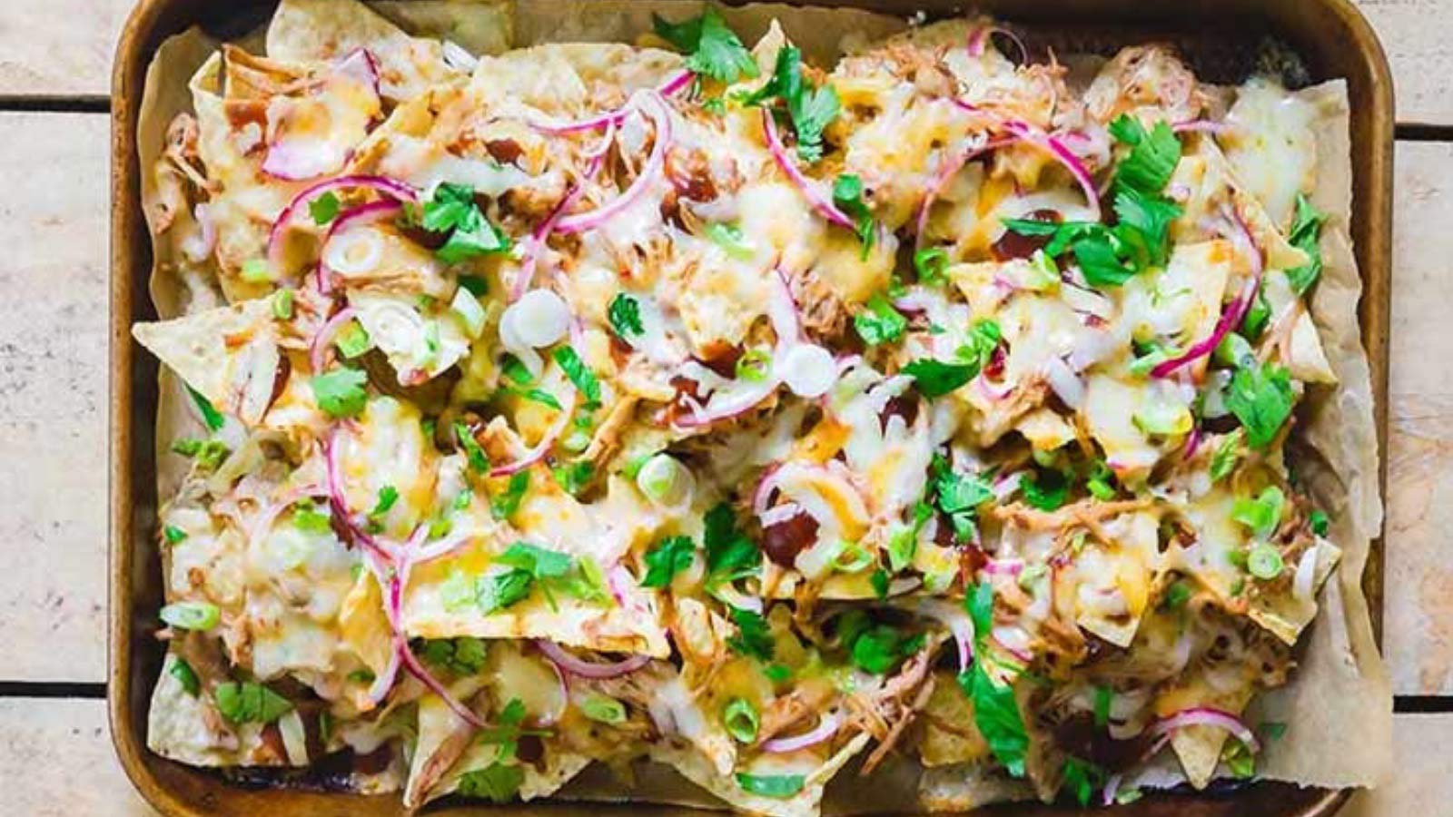 A sheet pan covered with BBQ pulled pork nachos.