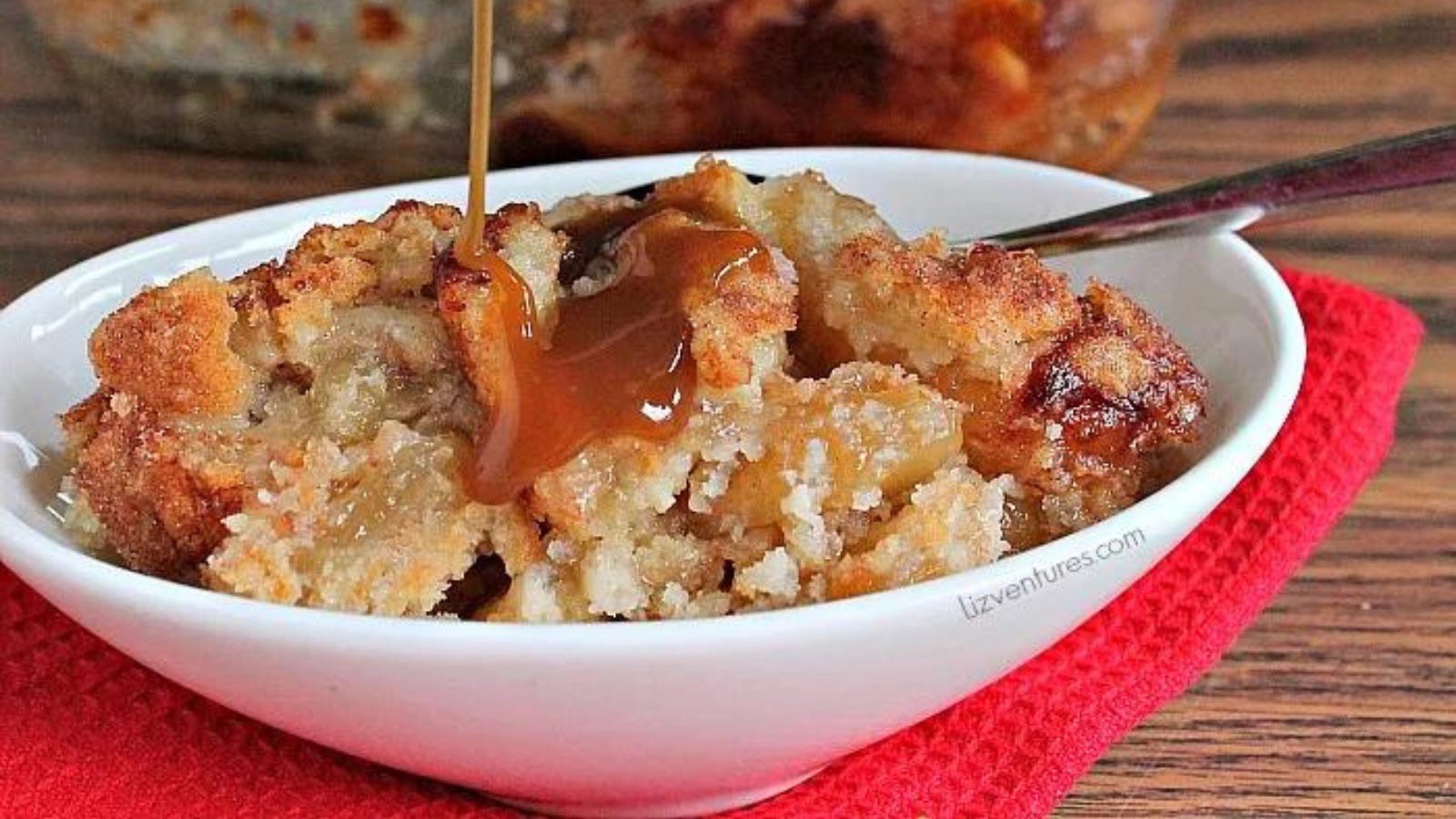 A white bowl filled with snickerdoodle cobbler is having caramel sauce drizzled over the top of the cobbler.