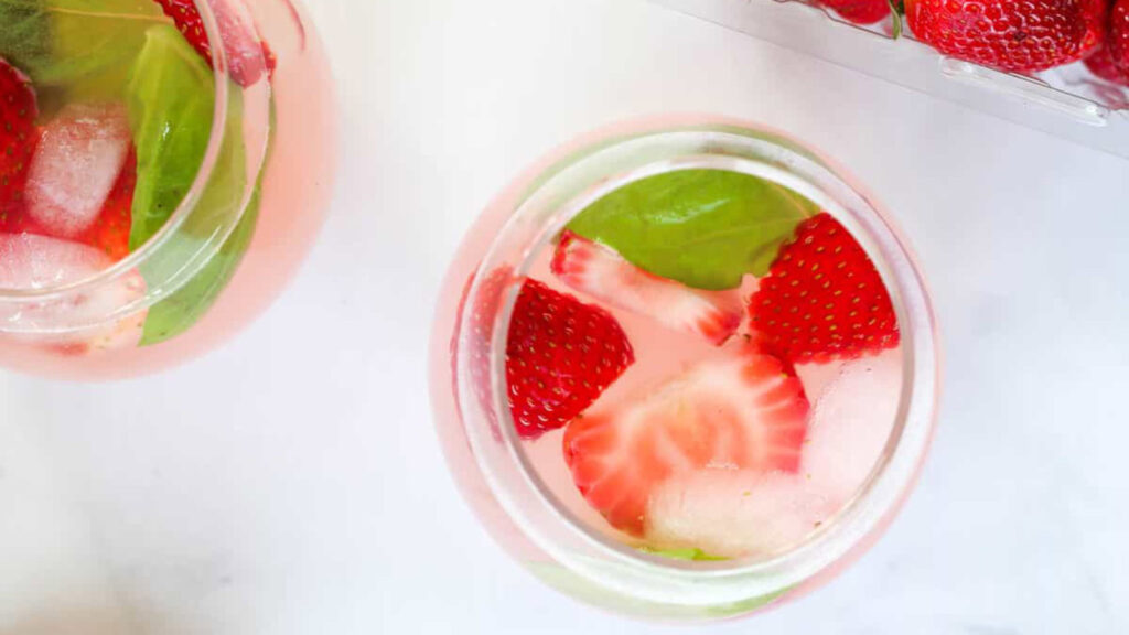 An overhead view of two glasses filled with fresh cut strawberries and strawberry mocktail spritzer.