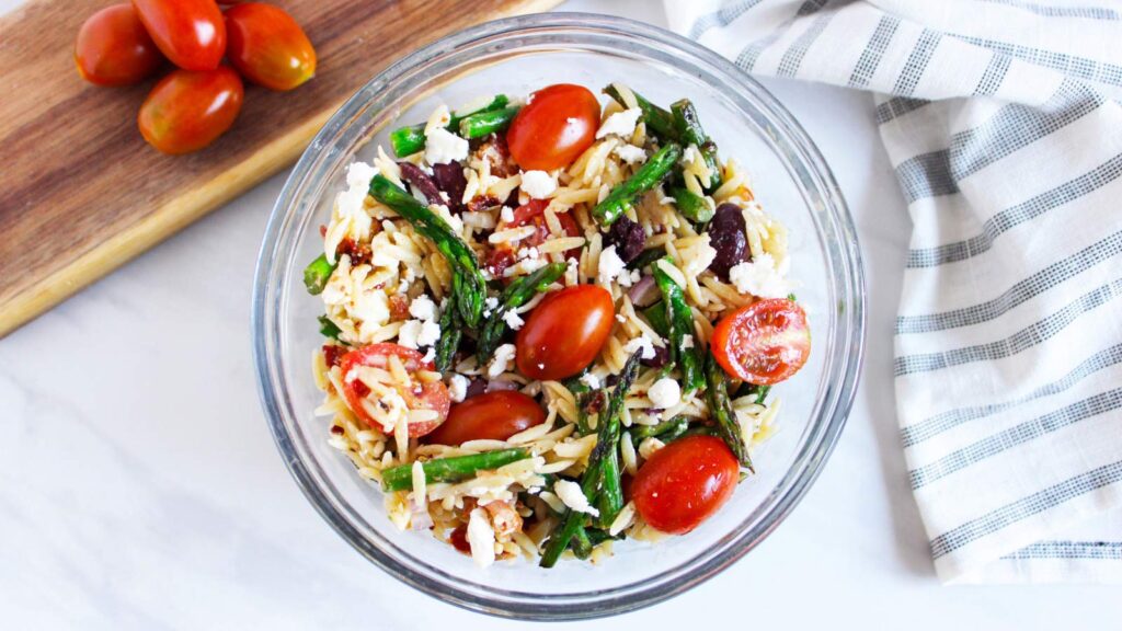 The mixed, finished, Asparagus Orzo salad with bacon in a glass bowl.