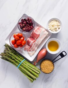 An overhead view of all the ingredients for this Asparagus Orzo With Bacon recipe on a white marble surface.