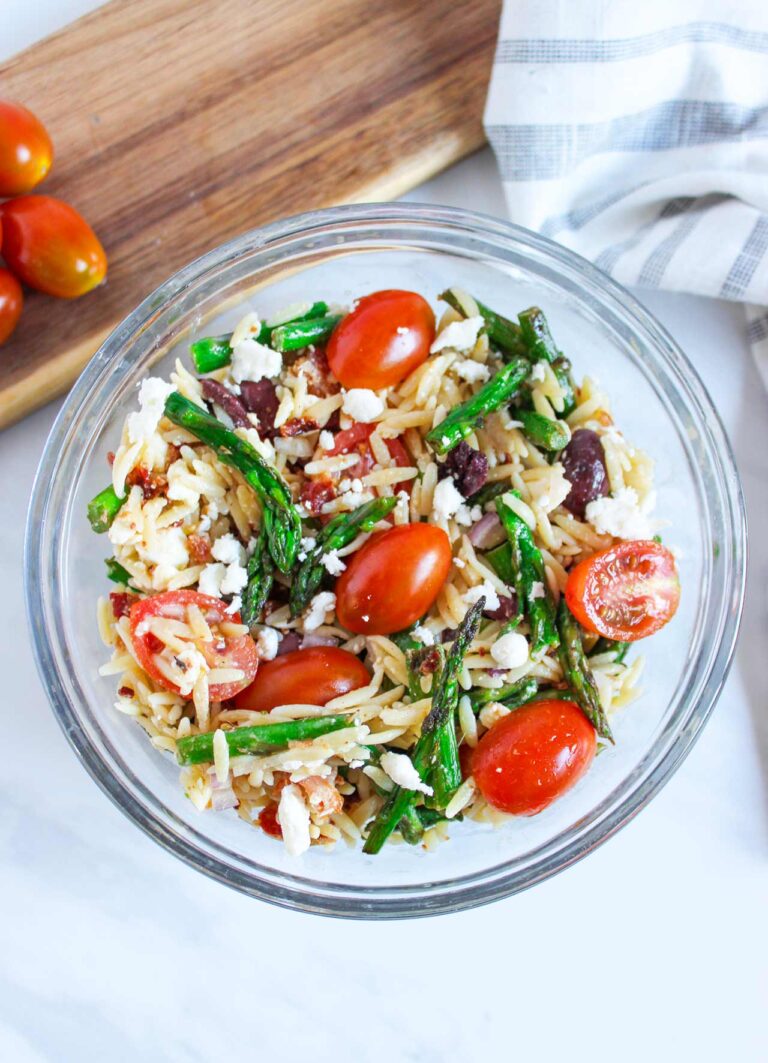 The mixed, finished, Asparagus Orzo salad with bacon in a glass bowl.