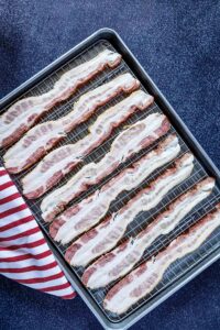 Uncooked bacon on a baking sheet. Dark background.