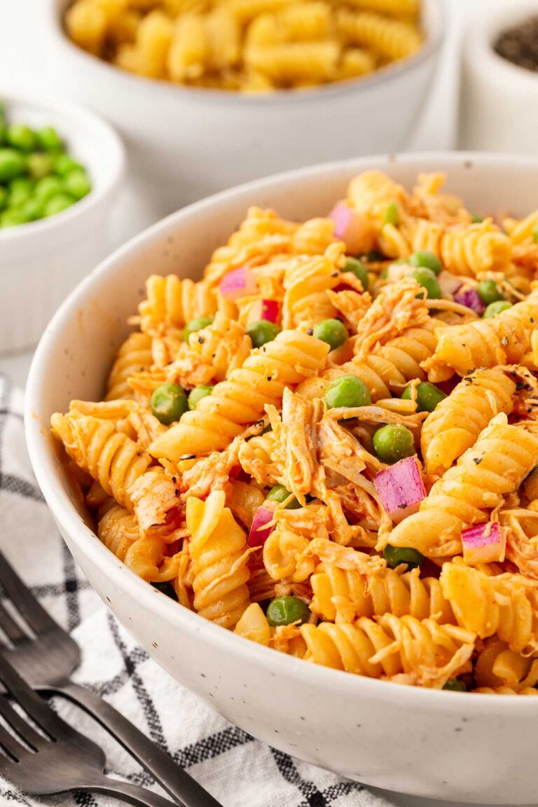 A side view of a white bowl filled with Buffalo Chicken Pasta Salad sitting on a table.