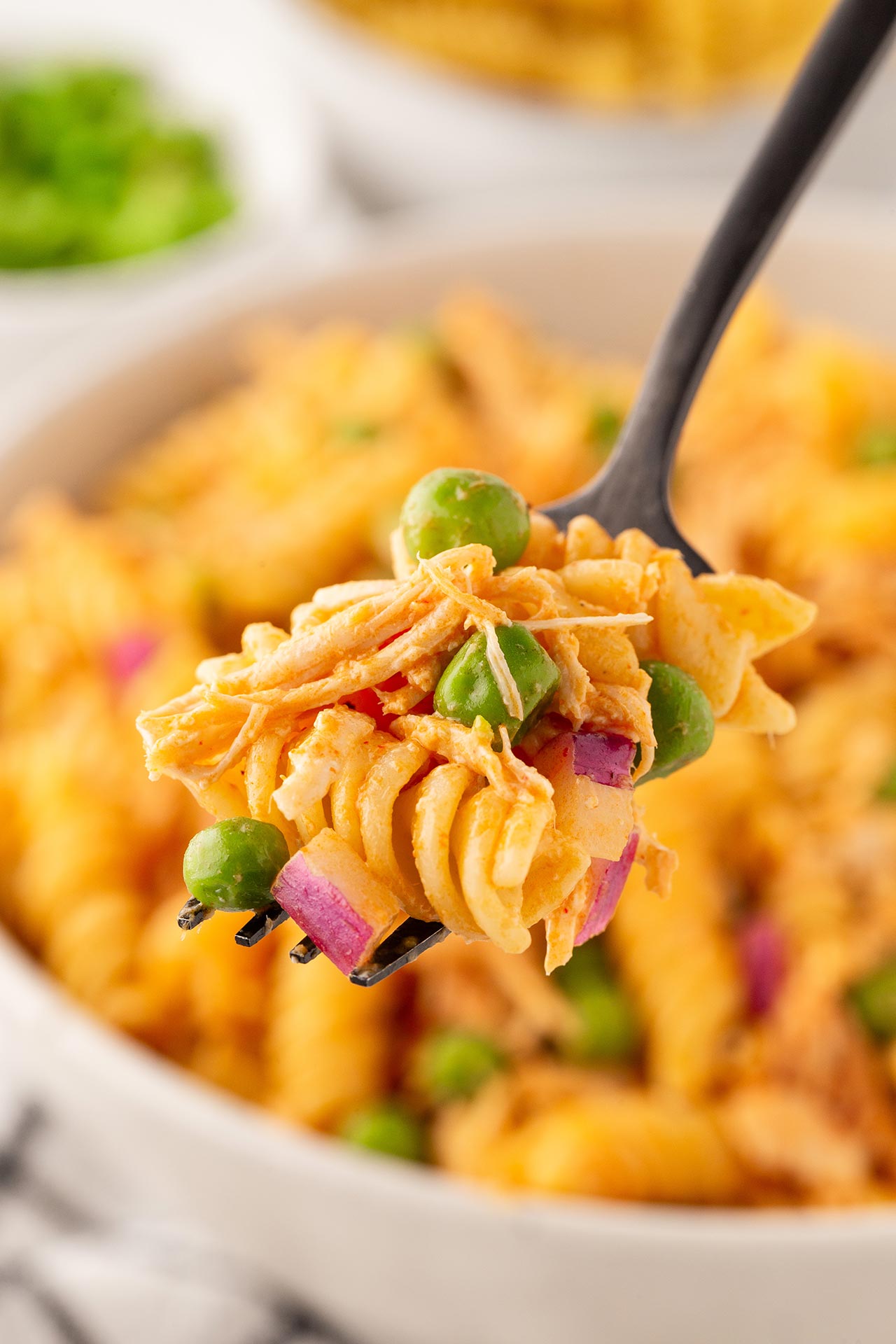 A fork lifts a forkful of Buffalo Chicken Pasta Salad up from a white bowl full of it.