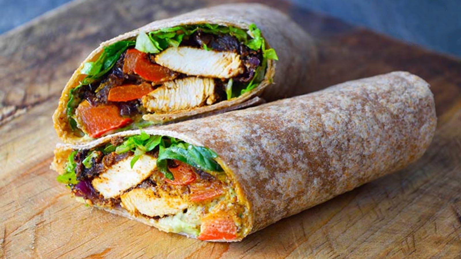 A Cajun Chicken Wrap cut in half and stacked up on a wood cutting board.