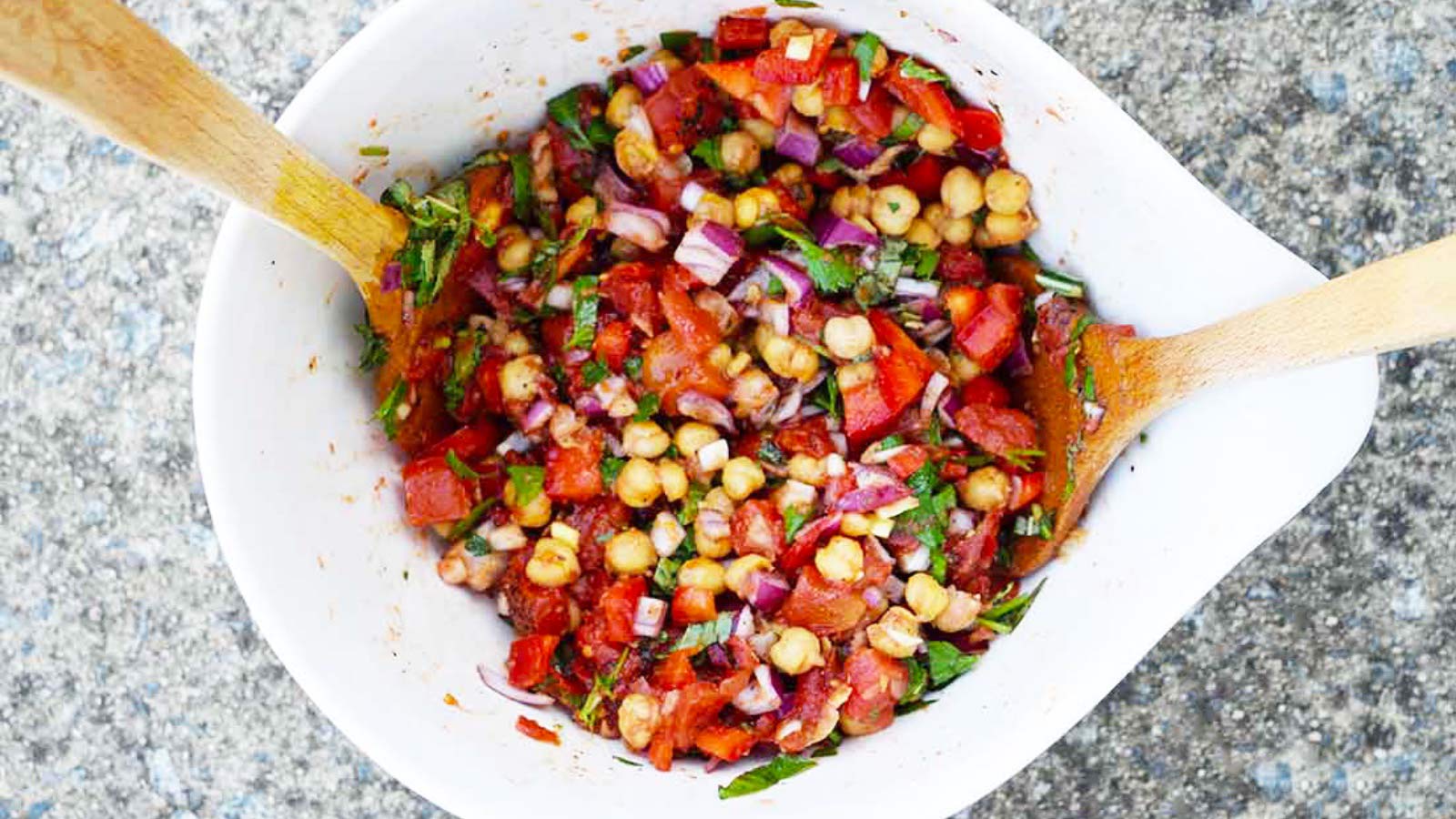 A large white mixing bowl with tongs in it sits halfway filled with chickpea salad.
