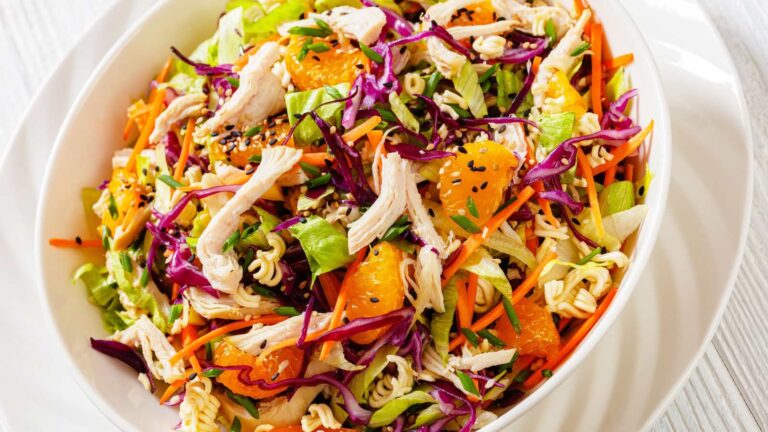 Chinese Chicken Salad with shredded chicken meat, mandarin oranges, crunchy noodles, red cabbage, napa cabbage, carrots, green onions in bowl, close-up.