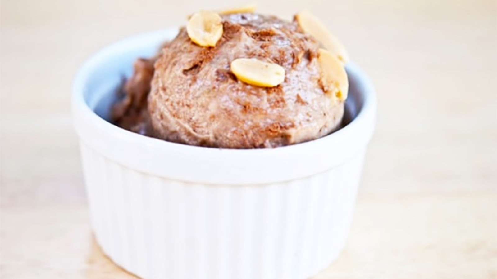 A scoop of chocolate peanut butter ice cream in a small white bowl, garnished with fresh peanuts.