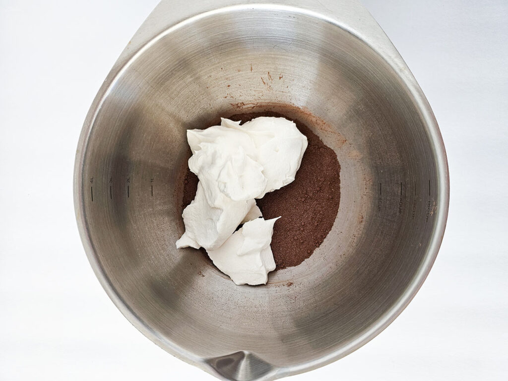 Whipped cream added to a mixing bowl with cocoa powder and sweetener.