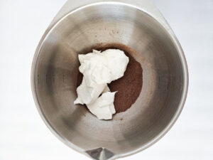 Whipped cream added to a mixing bowl with cocoa powder and sweetener.