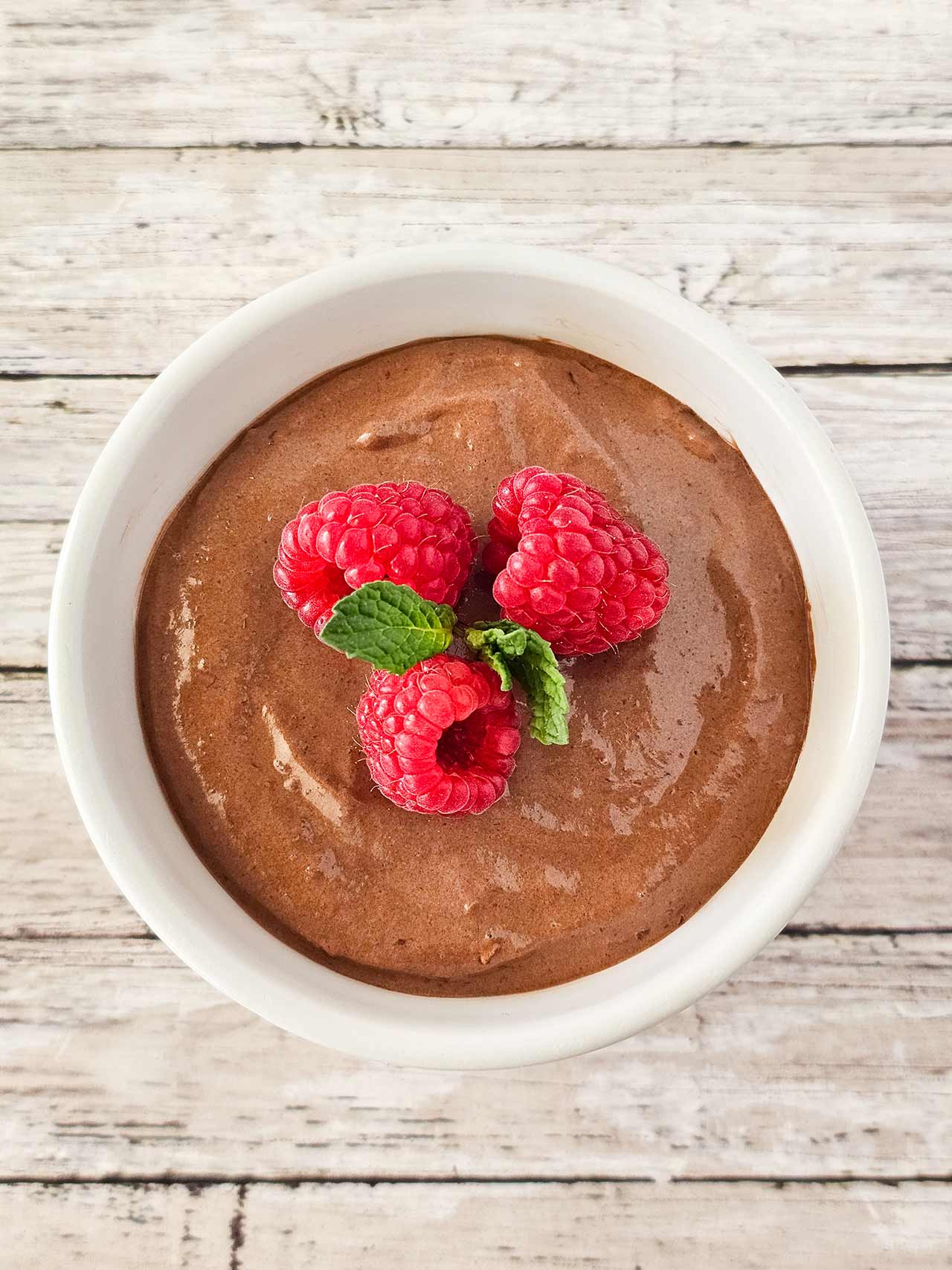 An overhead view of a white bowl filled with raspberry chocolate mousse.