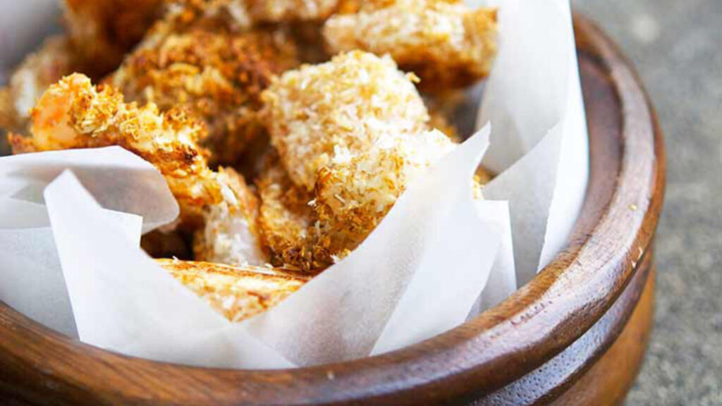 A wooden bowl with a parchment liner sits filled with golden brown popcorn shrimp.