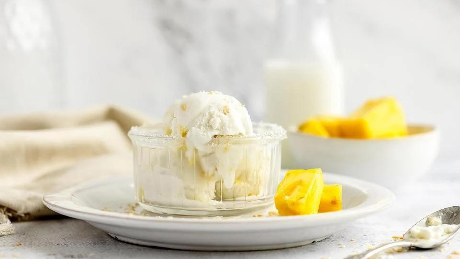 Three scoops of coconut pineapple frozen yogurt in a clear glass bowl, sitting on a white plate.