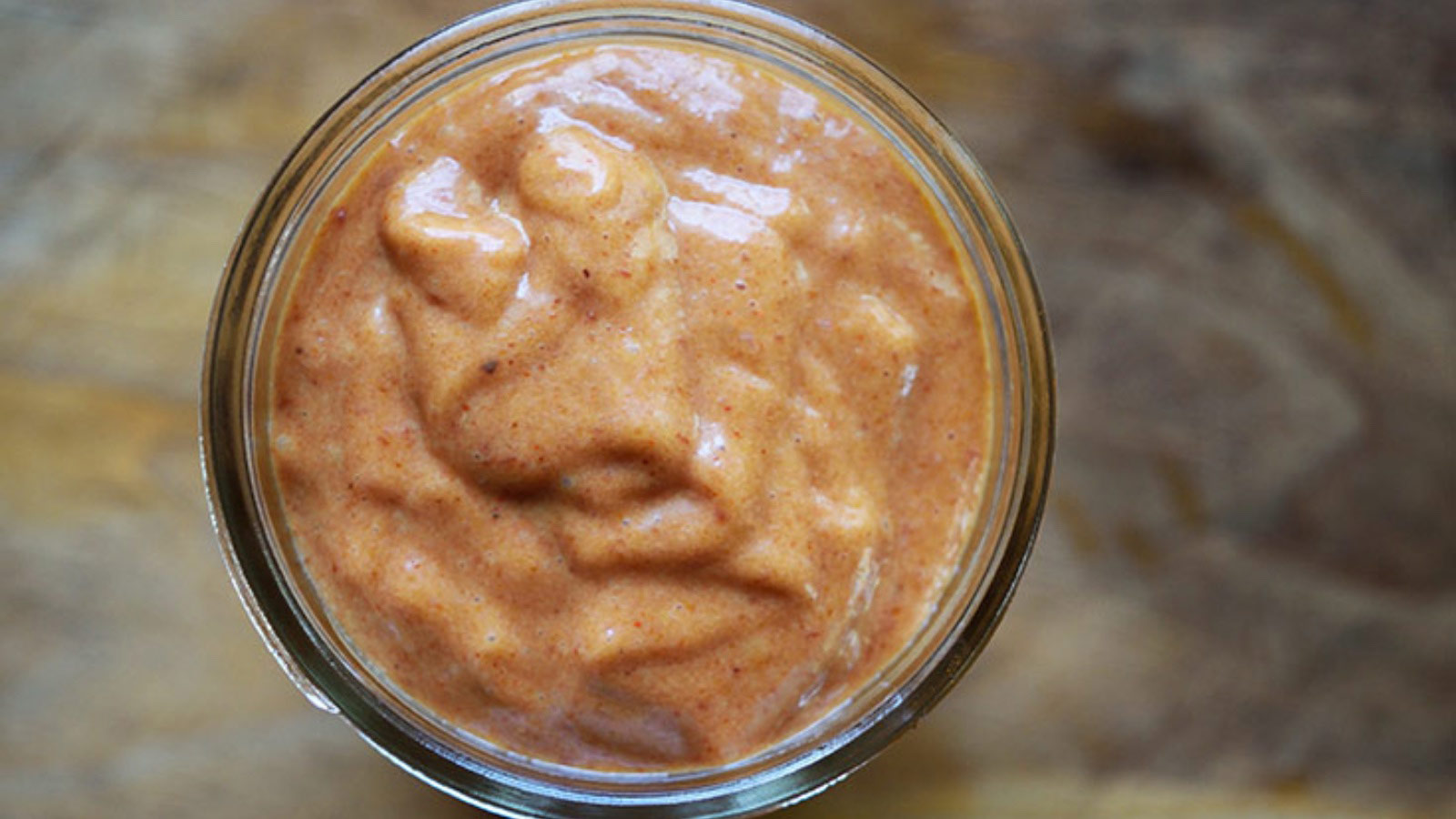 An overhead view of a small canning jar filled with Copycat Chick Fil A Honey BBQ Sauce.