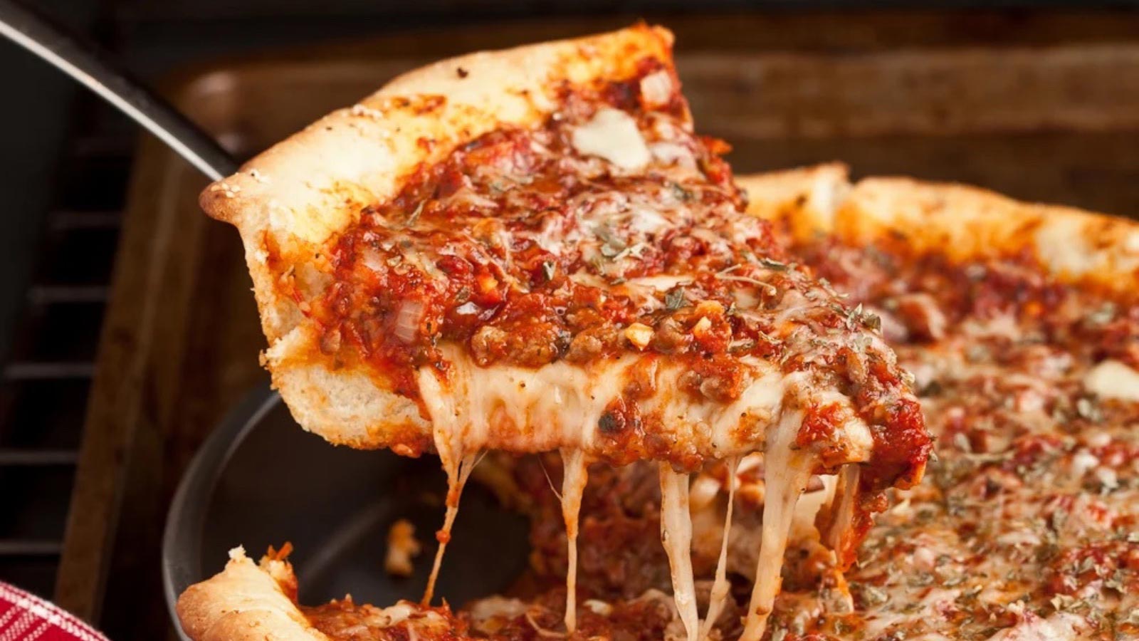 A spatula holds up a slice of Deep Dish Pizza.