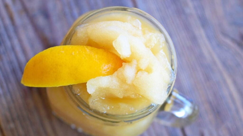 An overhead view of a frosty virgin coconut sugar margarita in a glass jar garnished with a lemon wedge on the rim of the jar.