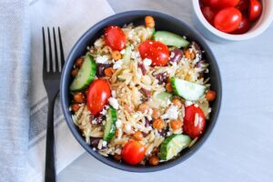 Overhead view of a black bowl filled with Greek Orzo Salad.
