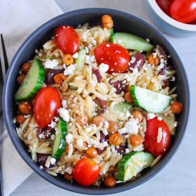 Overhead view of a black bowl filled with Greek Orzo Salad. A black fork lays to the left.
