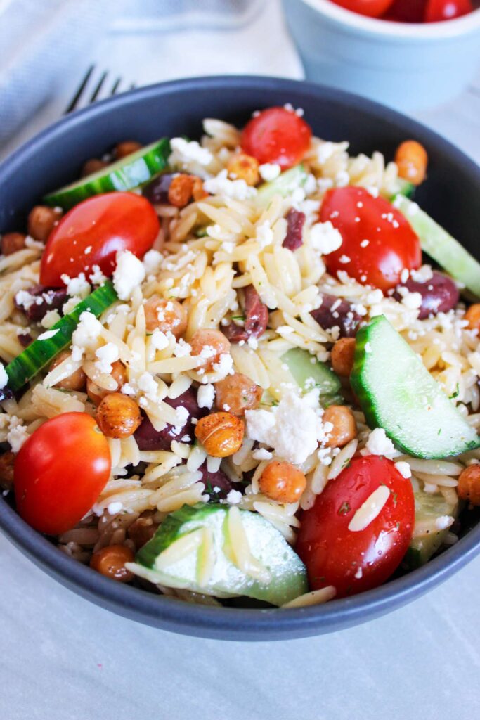 A side view of a black bowl filled with Greek Orzo Salad.