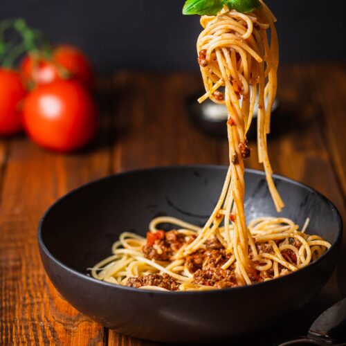 A fork lifts a twist of ground turkey spaghetti out of a black bowl.