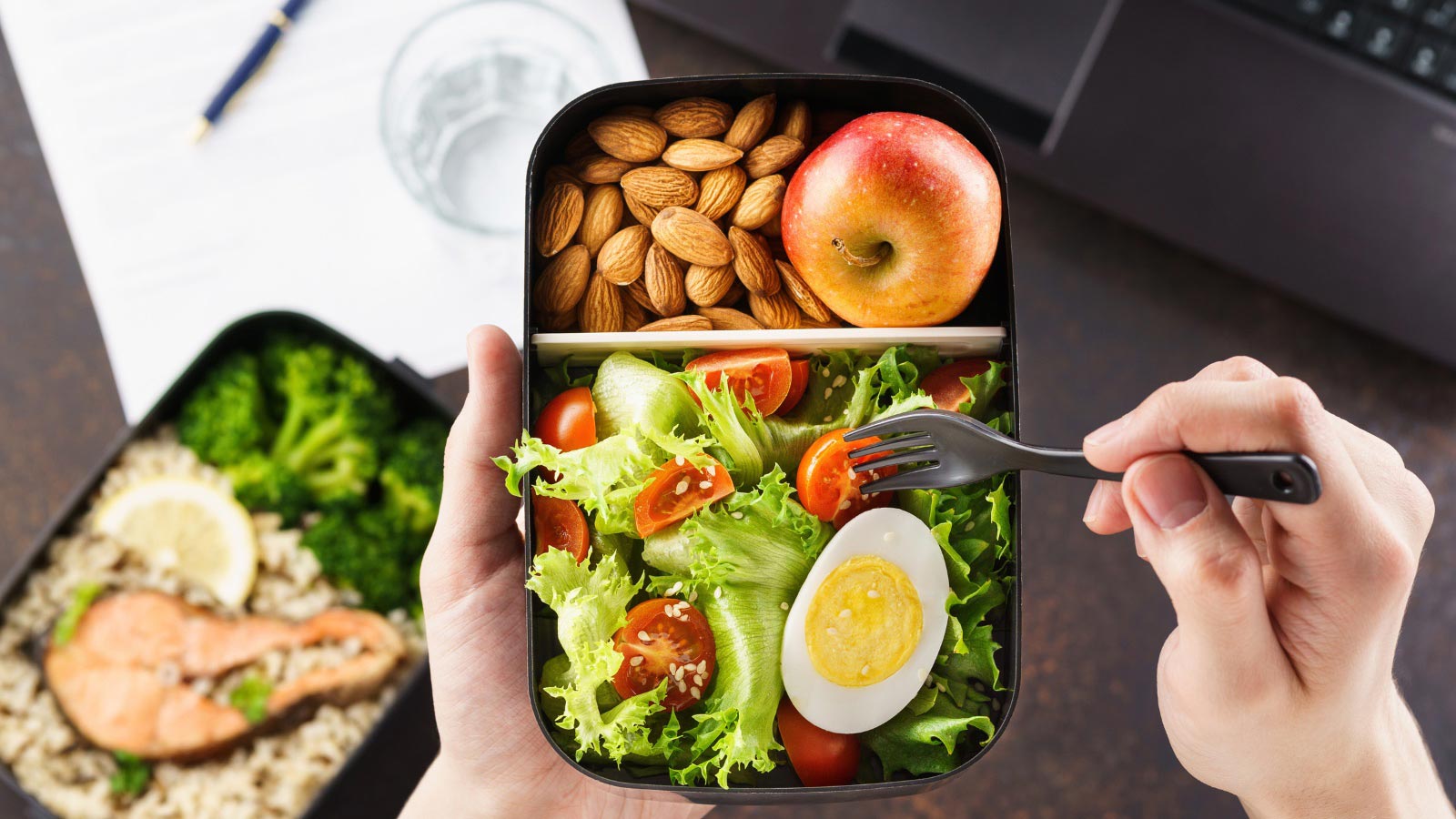 Healthy lunch at office workplace. Man eating nutrition lunch from lunch box at working table with laptop.