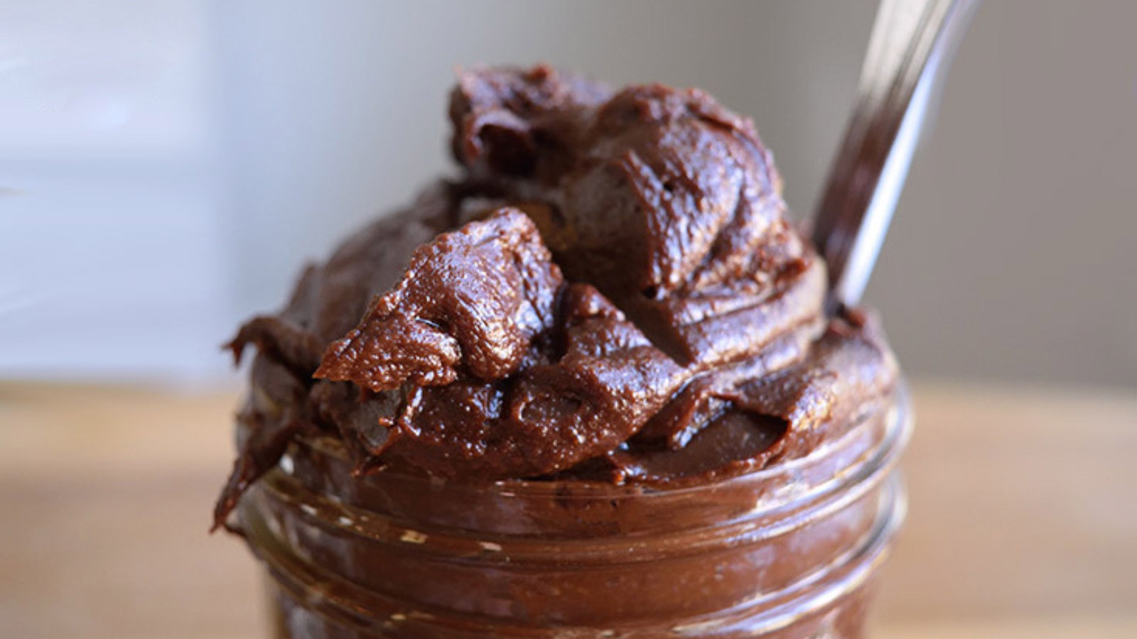 A closeup of an open jar over-filled with chocolate hazelnut spread.