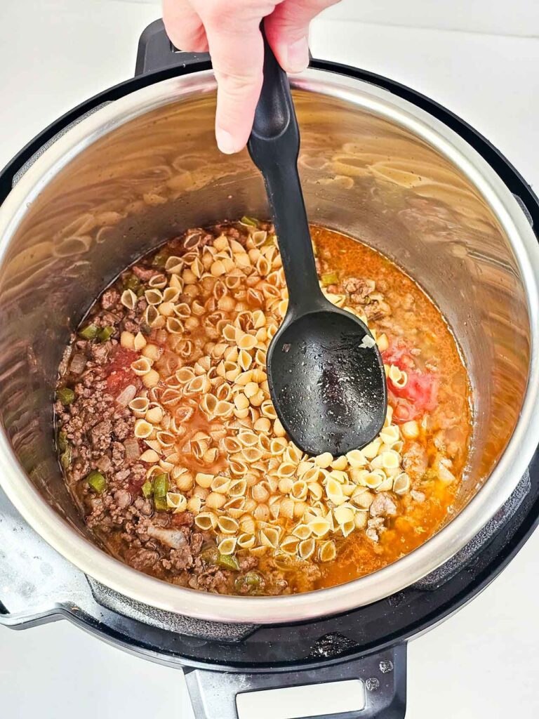 Stirring pasta shells into other ingredients in an Instant Pot.
