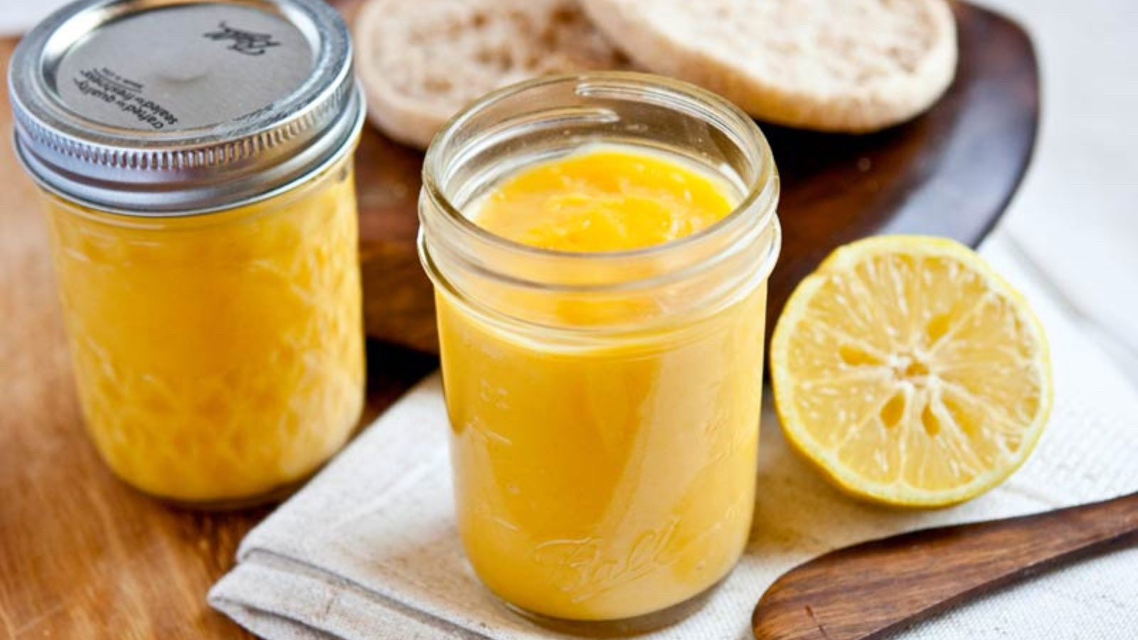 An open jar of lemon curd on a table with a second, closed jar and half a lemon.